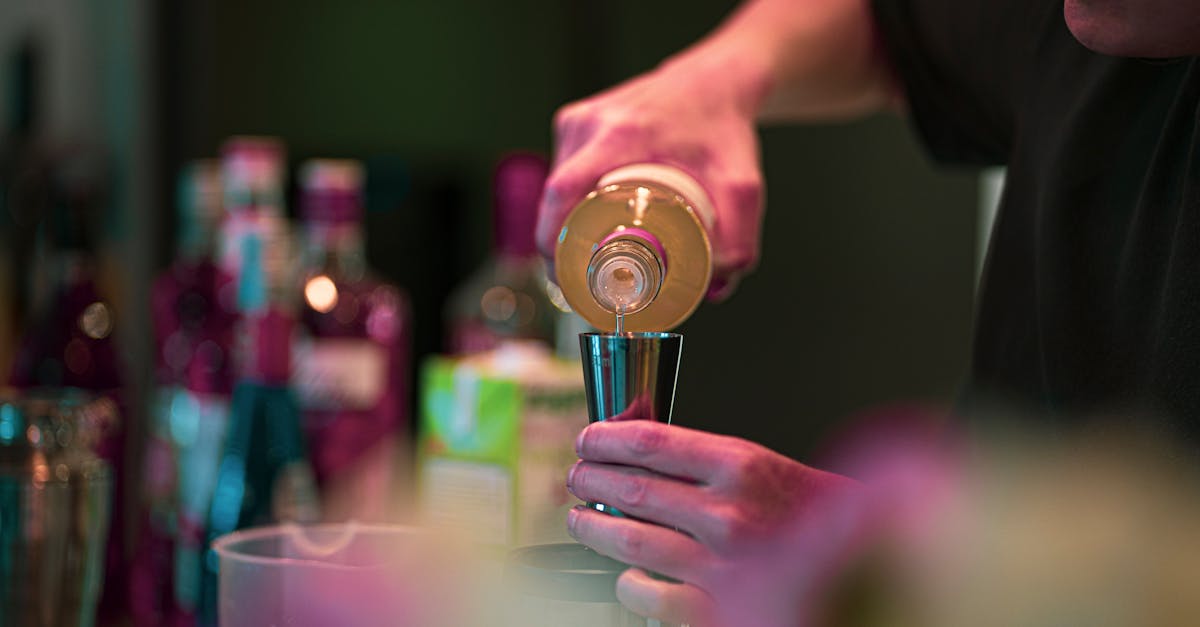 A bartender pouring a measure into a shaker at a moodily lit cocktail bar