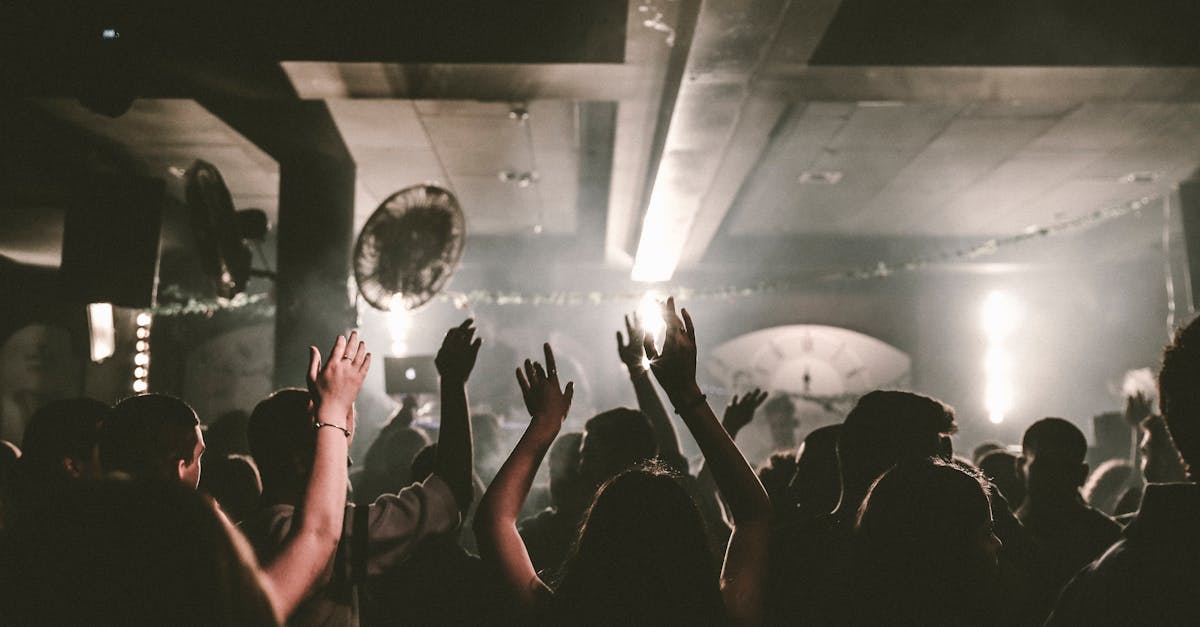 A packed nightclub dance floor with the crowd's arms raised under the lights
