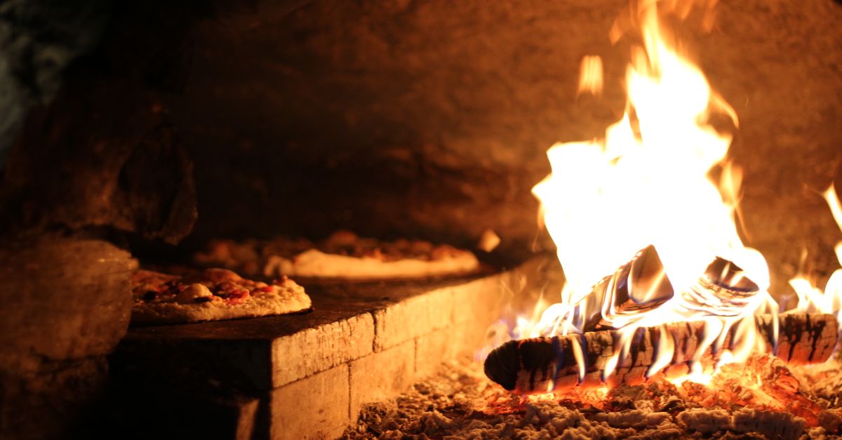 A wood-fired pizza oven with pizzas baking beside the flames